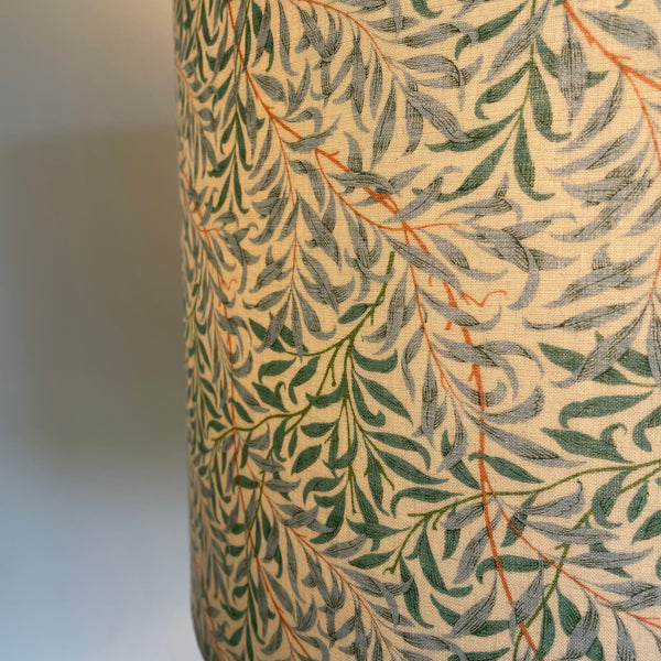 Close up of large drum hand crafted lamp shade in William Morris Willow and Boughs Cream fabric, lit.