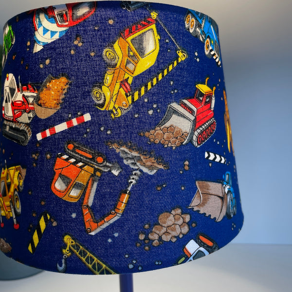 Small tapered hand crafted lamp shade with childrens' construction trucks fabric, lit, close-up..