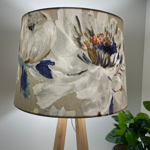 Close up of handcrafted fabric lampshade of bold rose pattern on dove grey background on natural wood lamp base, lit.