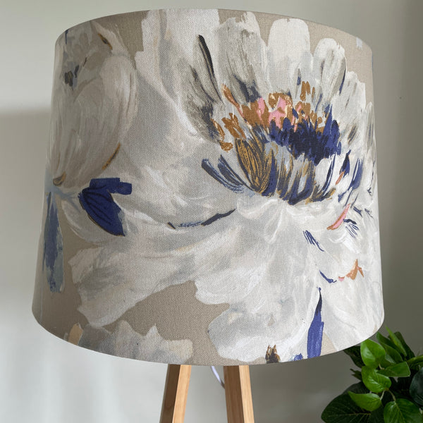 Close up of handcrafted fabric lampshade of bold rose pattern on dove grey background on natural wood lamp base, unlit.