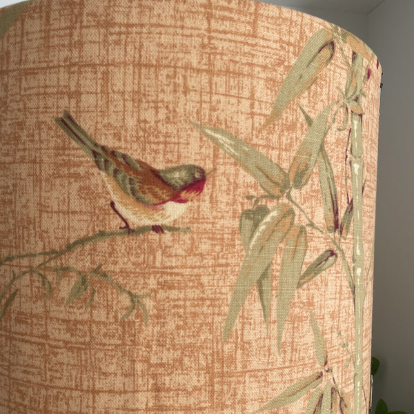 Close up of delicate bird perched on bamboo on large drum lamp shade.