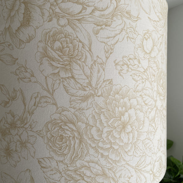 Close up of large drum fabric light shade with flowers etched in gold on cream background, unlit.