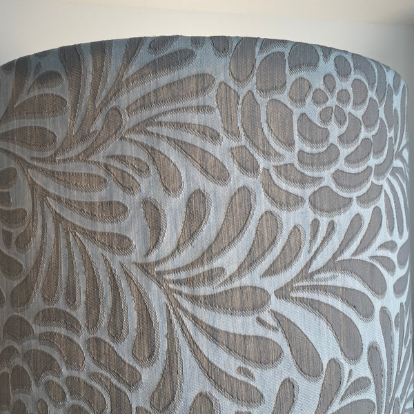 Top edge of Large fabric light shade with large taupe flowers and foliage on silver grey background, lit.