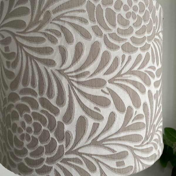 Close up of large fabric light shade with large taupe flowers and foliage on silver grey background, unlit.