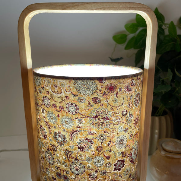 Close up of scandi style natural wood table lamp with eastern paisley fabric on light shade. Lit.