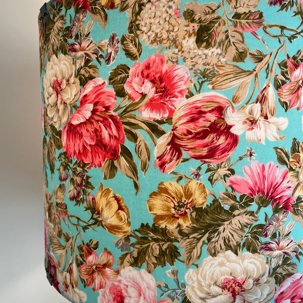 Close up of large drum fabric lamp shade with flowers on blue background, lit. 