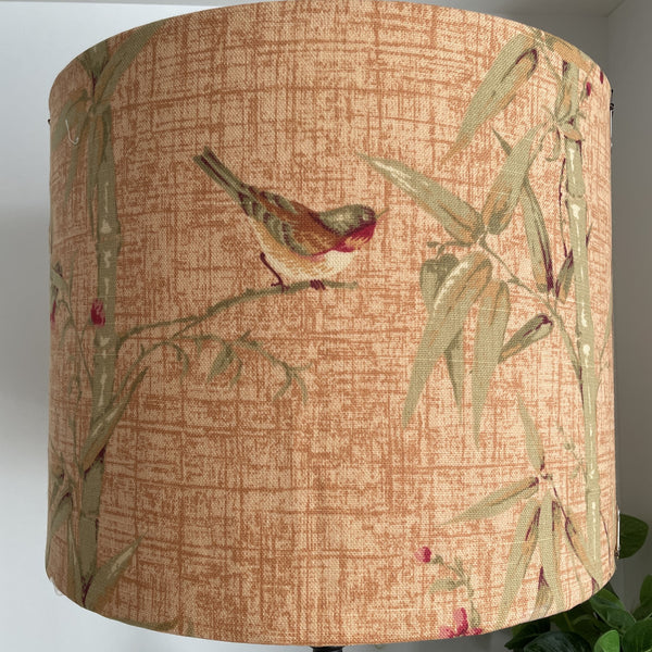 Delicate bird perched on bamboo on large drum lamp shade, unlit.