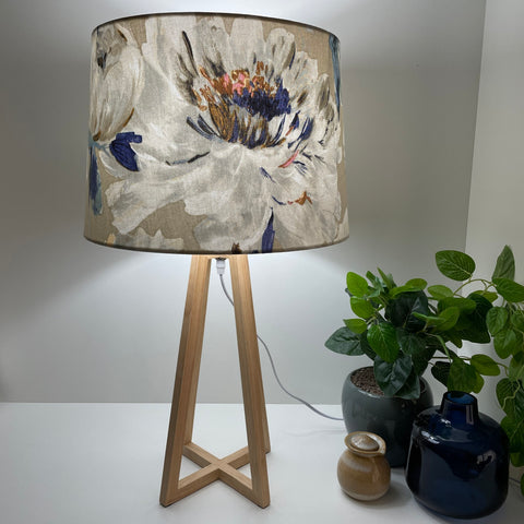 Handcrafted fabric lampshade of bold rose pattern on dove grey background on natural wood lamp base, lit.