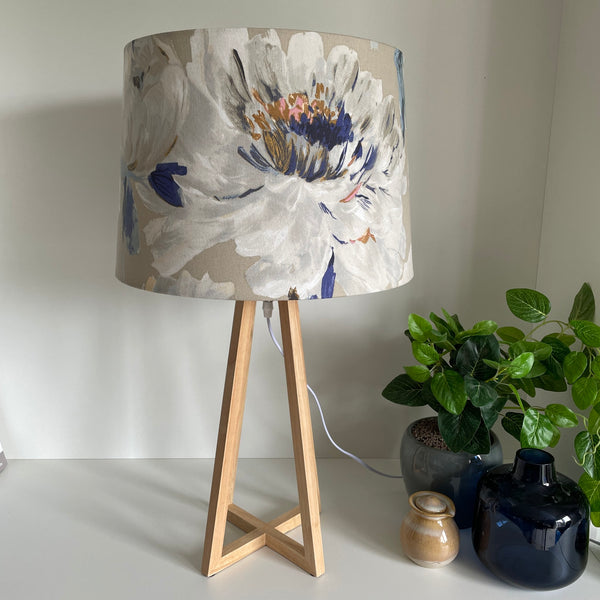 Handcrafted fabric lampshade of bold rose pattern on dove grey background on natural wood lamp base, unlit.