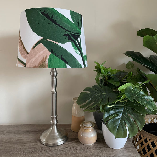 Hand crafted fabric lamp shade with large leaves on crisp white background, unlit on brushed chrome lamp base.