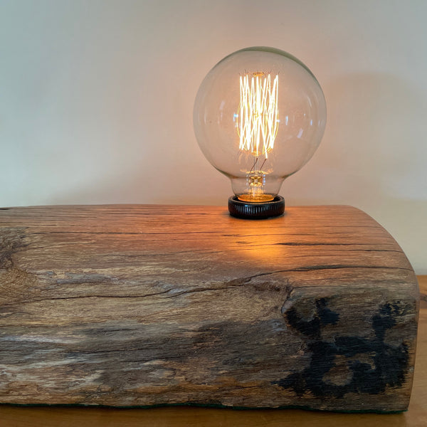 Handcrafted wharf timber table lamp with edison light bulb, lit, close up of glow from bulb and front edge.