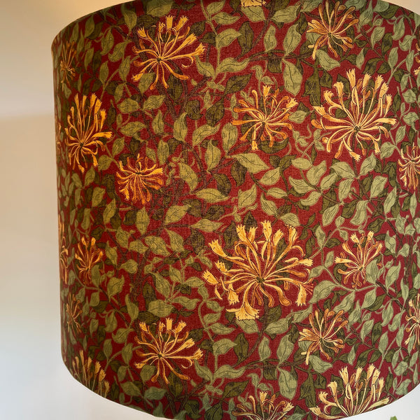 Close up of large barrel handcrafted lampshade with William Morris honeysuckle deep red fabric, lit.