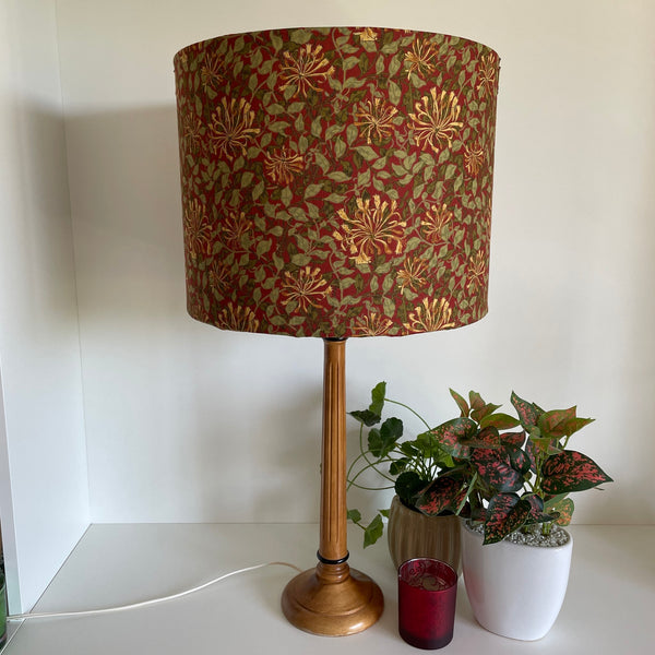 Large barrel handcrafted lampshade with William Morris honeysuckle deep red fabric, unlit on wooden stand.