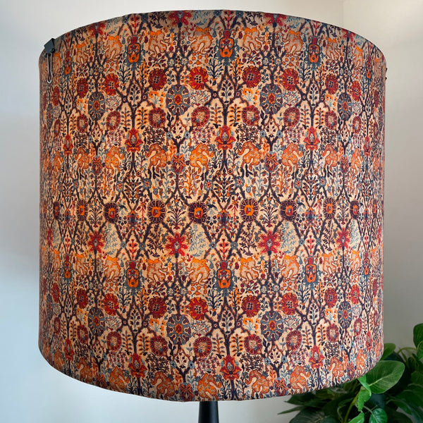 Large drum fabric light shade in warm reds and oranges in a paisley pattern, lit.