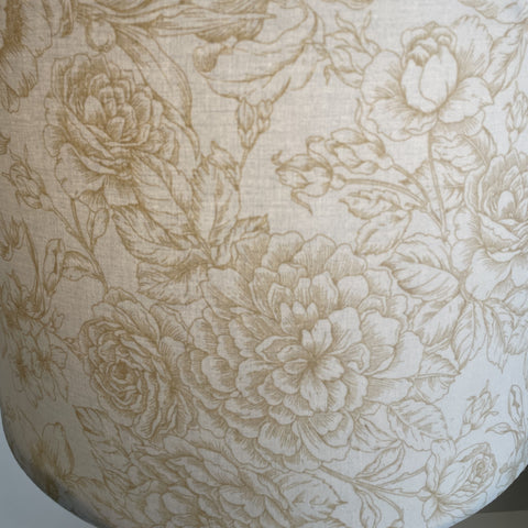 Large drum fabric light shade with flowers etched in gold on cream background, lit.