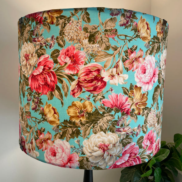 Large drum fabric lamp shade with flowers on blue background, lit. 