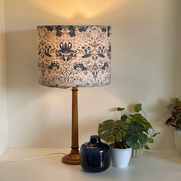 Large drum handcrafted lamp shade with William Morris fabric, lit on a wooden stand..