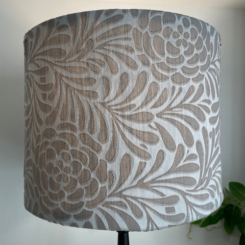 Large fabric light shade with large taupe flowers and foliage on silver grey background, lit.