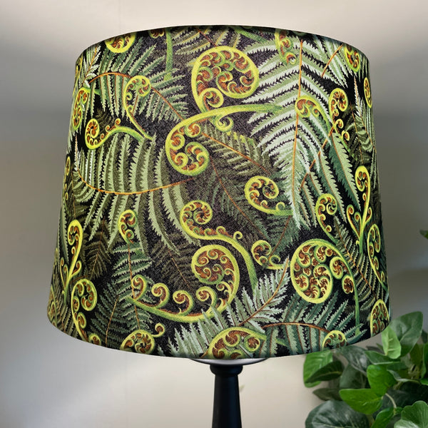 Large tapered hand crafted lamp shade with green fern fabric, close up, lit.