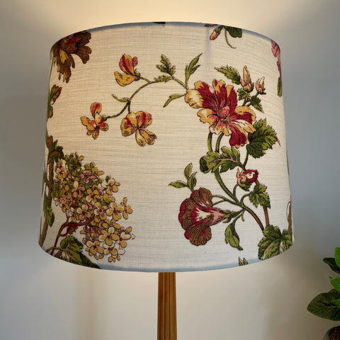 Large tapered fabric lamp shade with flowers on a white background, lit.