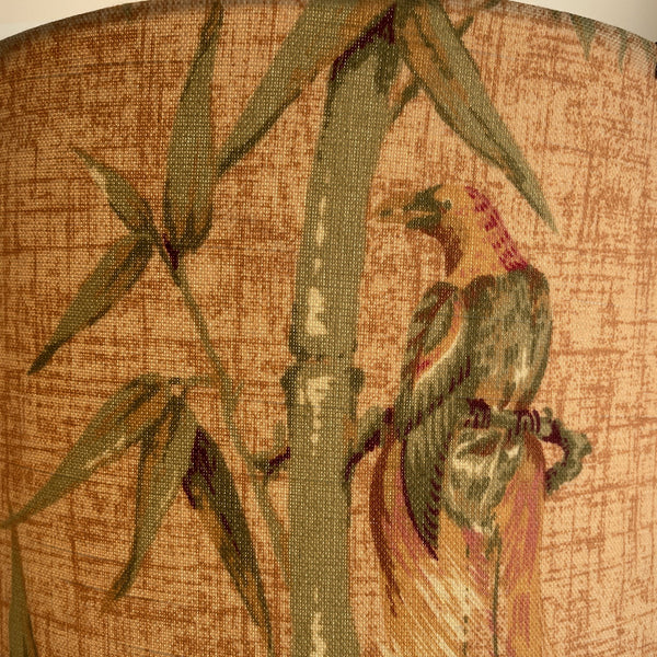 Large tropical bird perched on bamboo, close up of fabric large drum lamp shade, lit.