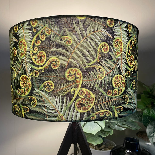 Medium barrel hand crafted lamp shade with green fern fabric, close up, lit.