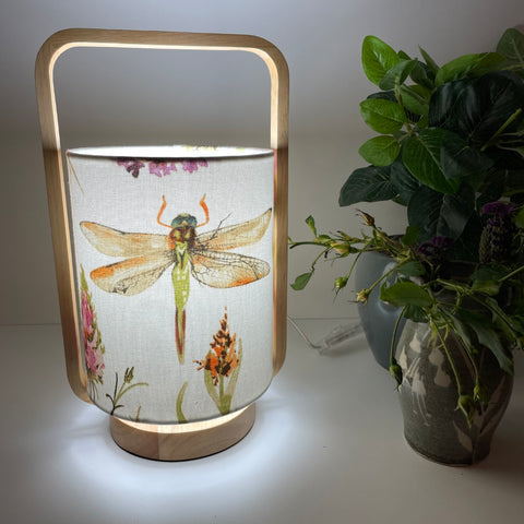 Natural timber table lamp with dragonfly fabric lampshade, lit.