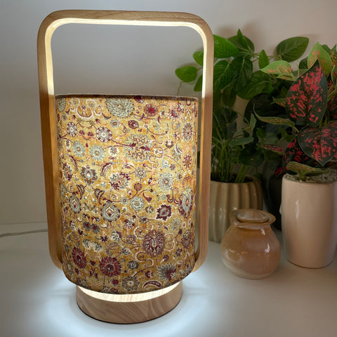 Natural wood table lamp with bespoke fabric lamp shade, lit.