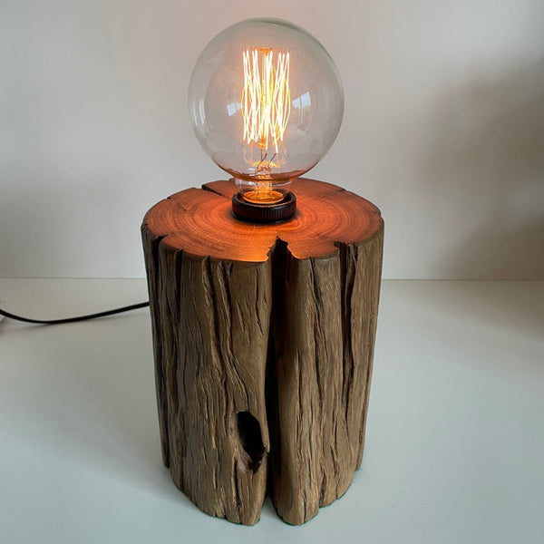 Round timber table lamp with front hole and polished top. Lit.