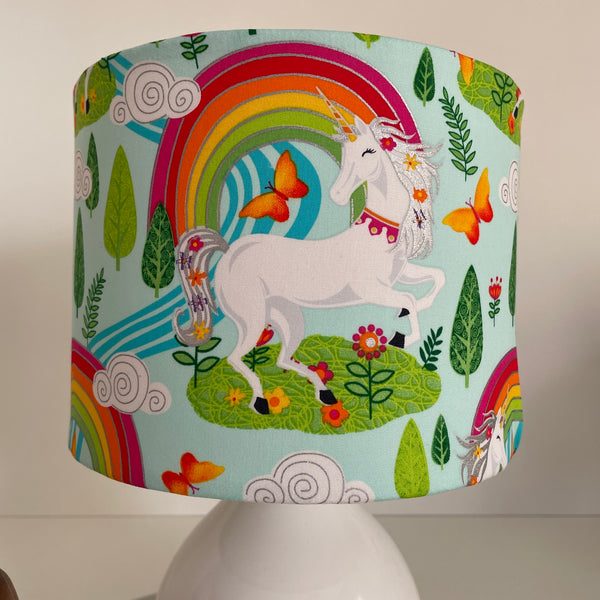 Small drum fabric lamp shade with white unicorn and orange butterflies, on white base, unlit, close up..