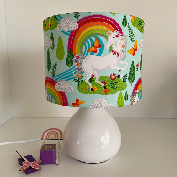 Small drum fabric lamp shade with white unicorn and orange butterflies, on white base, unlit.