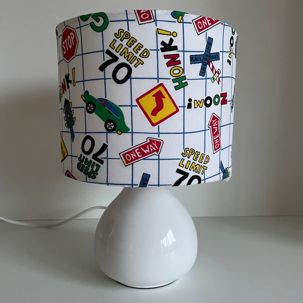 Small fabric hand crafted lamp shade with fun road signs and cars on white background, unlit.