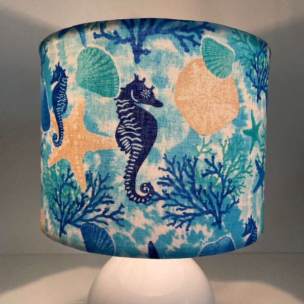 Small handcrafted drum lamp shade with sea horse and star fish fabric on white base, lit, close up