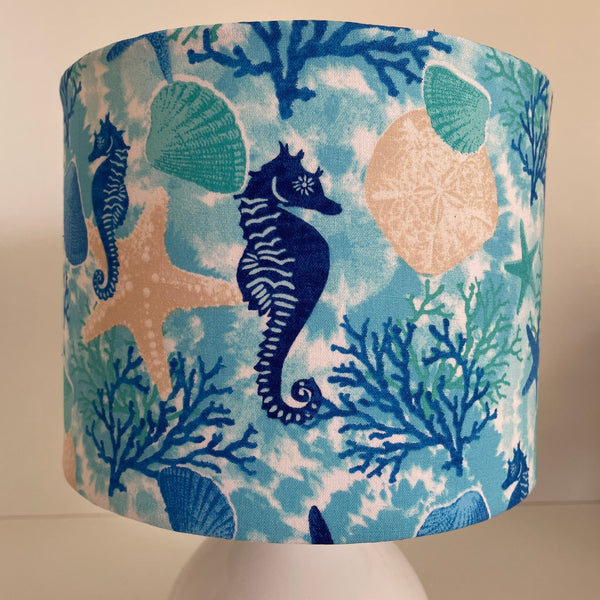 Small handcrafted drum lamp shade with sea horse and star fish fabric on white base, unlit, close up.t.