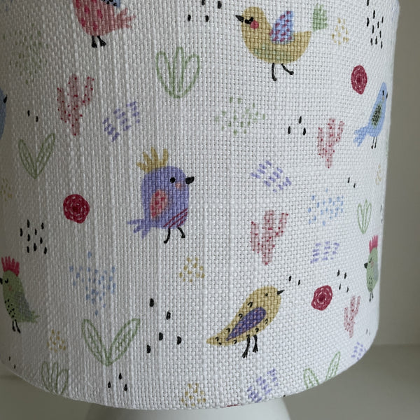 Small hand crafted lamp shade with sweet birdies on a white background lamp shade, unlit, close up.