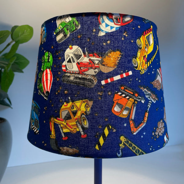 Small tapered hand crafted lamp shade with childrens' construction trucks fabric, lit.
