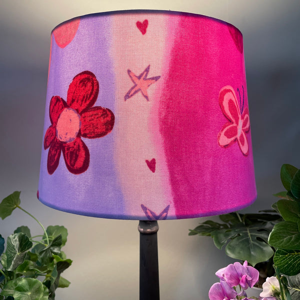 Medium tapered handcrafted fabric lampshade in a variety of pinks with flowers and butterflies.