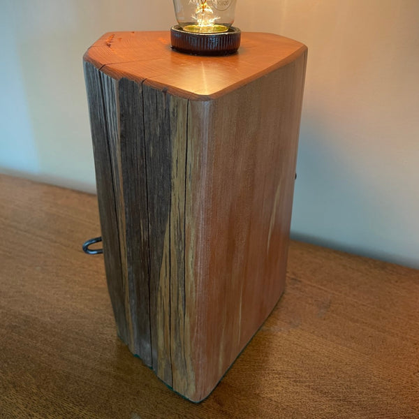 Bees wax polished top and smooth edge with glow of edison light bulb on unique wooden table lamp, handcrafted from old totara post.
