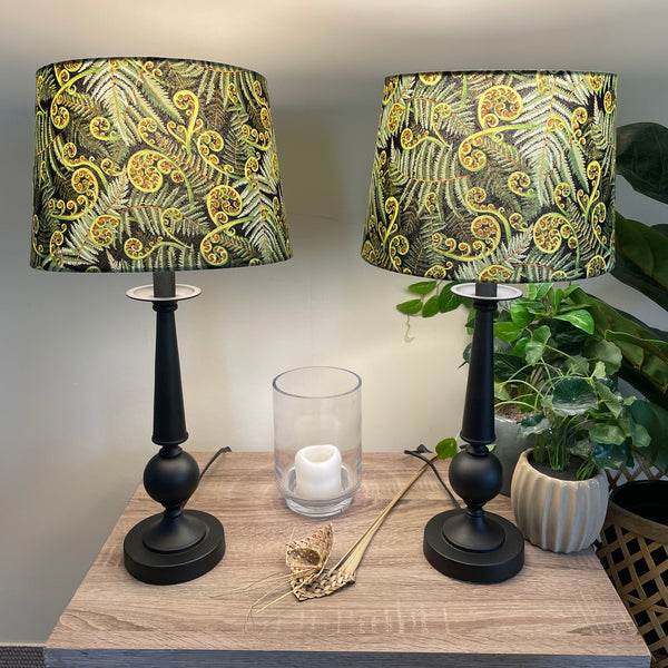 Two large tapered hand crafted lamp shades with green fern fabric, close up, lit.