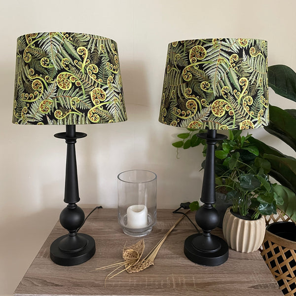 Two large tapered hand crafted lamp shades with green fern fabric, close up, unlit.