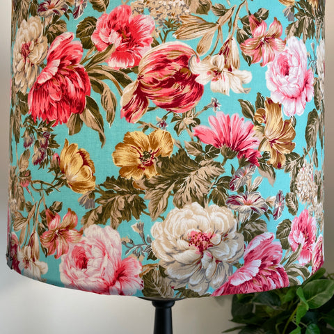 Variety of white, pink and gold flowers on handcrafted fabric lamp shade, lit.