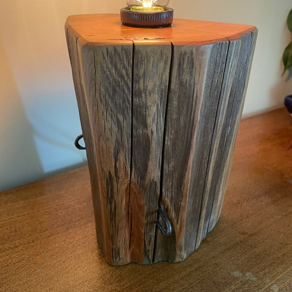 Polished grain with glow of edison light bulb on unique wooden table lamp, handcrafted from old totara post.