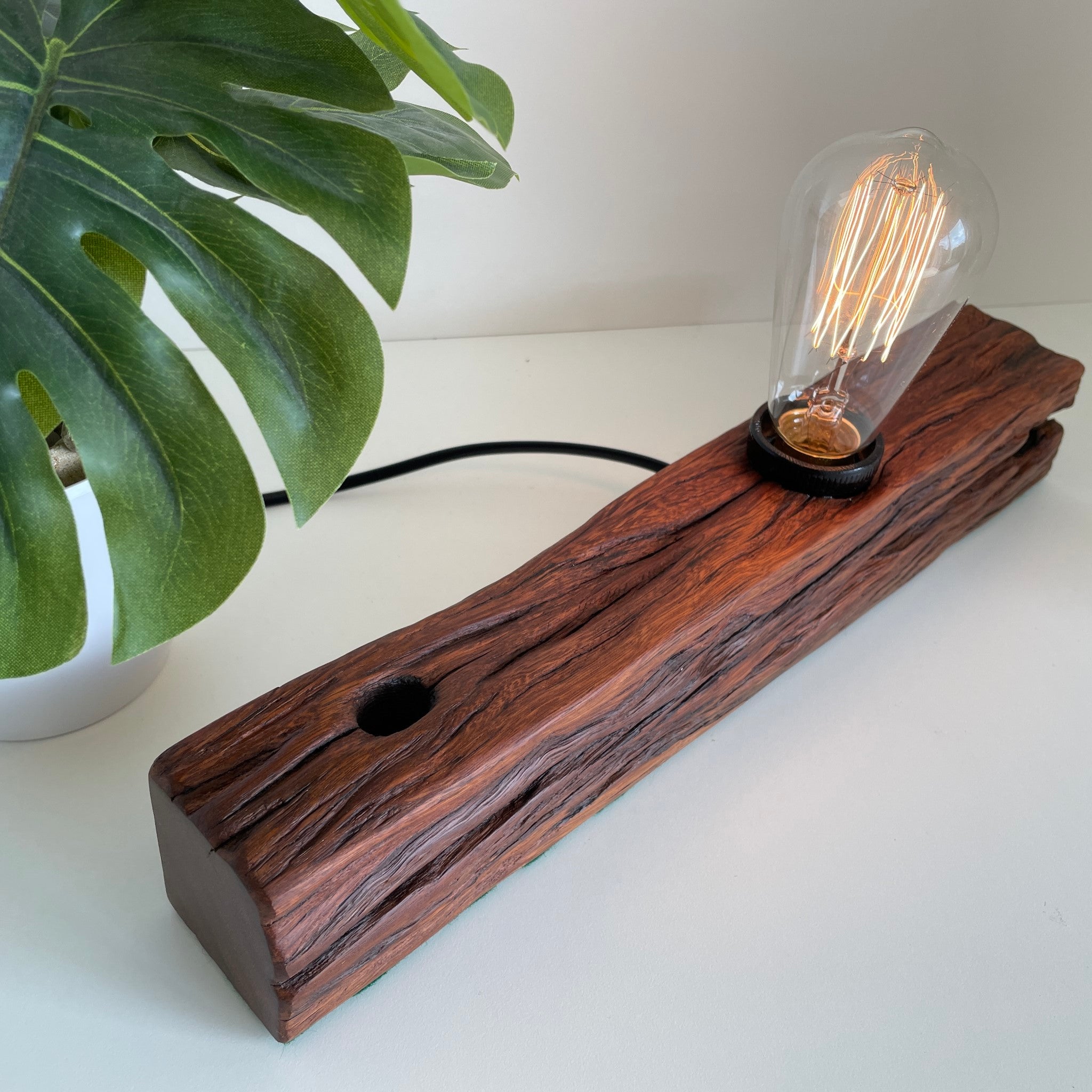 Wooden table lamp handcrafted from old telegraph post with edison bulb, lit.