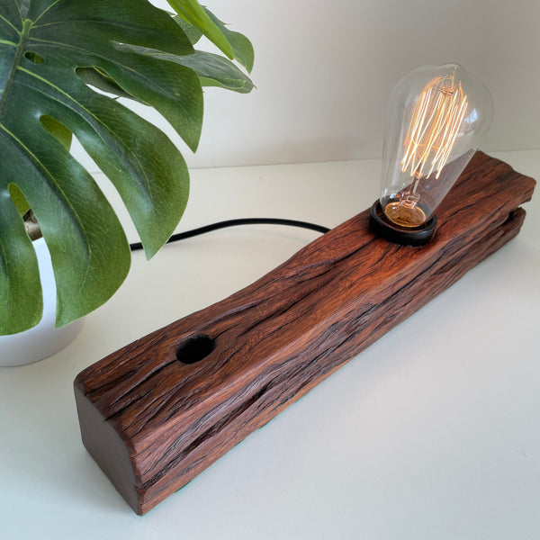 Wooden table lamp handcrafted from old telegraph post with edison bulb, lit.