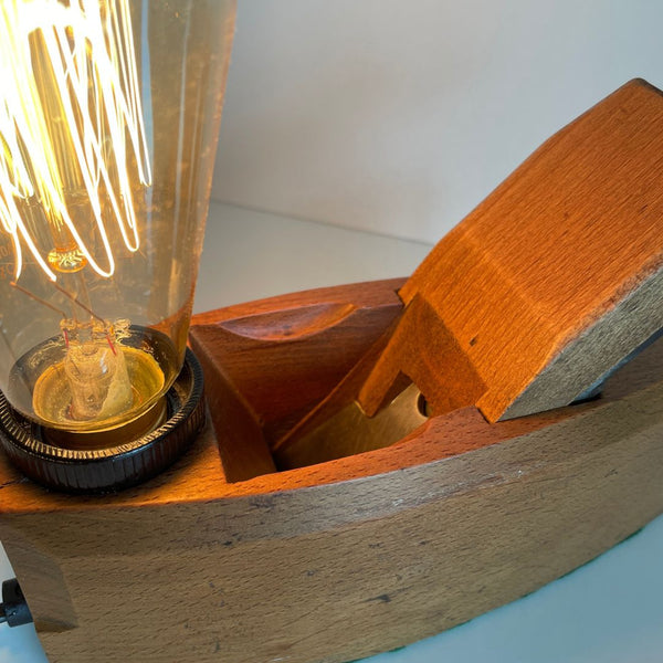 Wood table lamp with edison light bulb and old carpenter's wood plane, lit, close up.