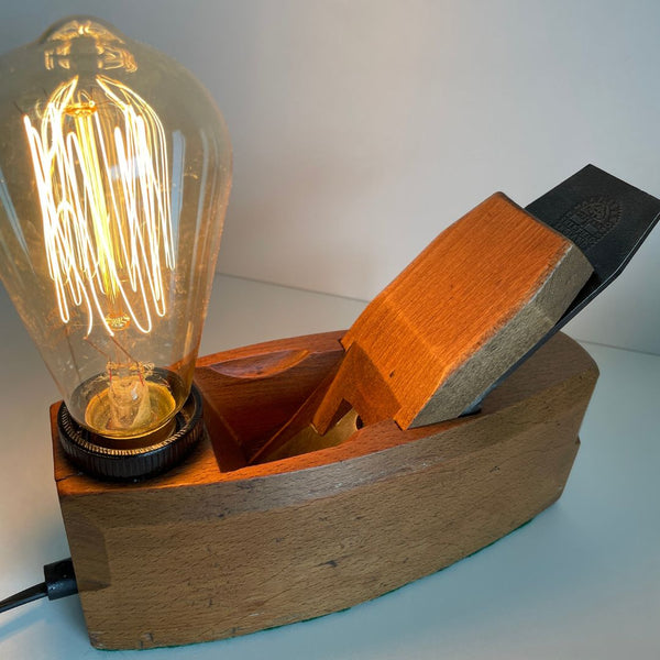 Wood table lamp with edison light buln and old carpenter's wood plane, side view, lit.